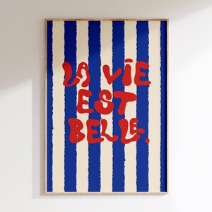 May include: A poster with blue and white stripes and the text "La vie est belle" in red.