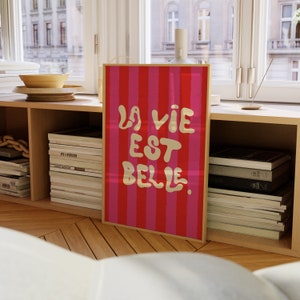 May include: A framed print with a red and pink striped background and the text "La vie est belle" in gold lettering.