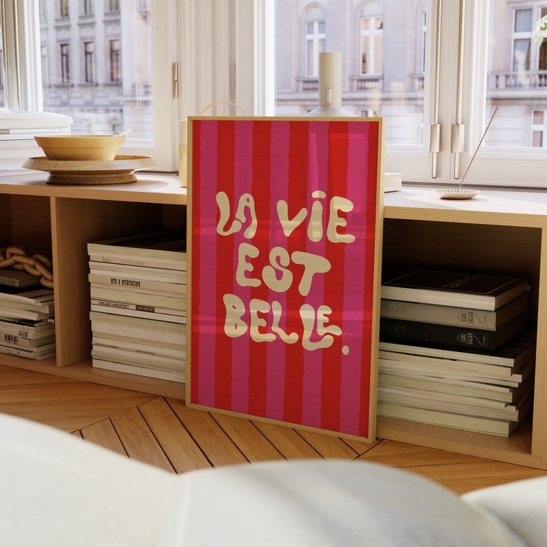 May include: A framed print with a red and pink striped background and the text "La vie est belle" in gold lettering.