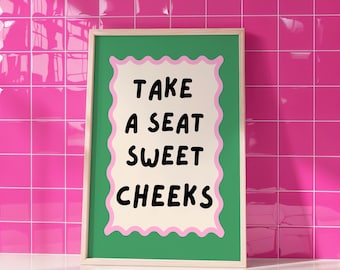 Może przedstawiać: Oprawiony wydruk z napisem "TAKE A SEAT SWEET CHEEKS" w czarnym kolorze. Tekst znajduje się na kremowym tle z różową, falistą obwódką, na zielonym tle. Rama jest w jasnym kolorze drewna.