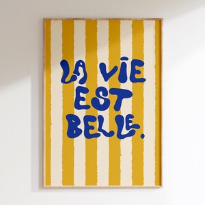May include: A yellow and white striped poster with the text "La vie est belle" in blue.