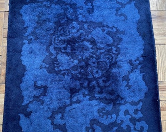 May include: A blue and black patterned rug with a fringed edge. The rug has a dark blue background with a lighter blue pattern of swirling shapes.