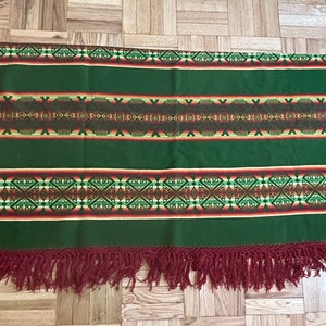 May include: A green and red woven blanket with a geometric pattern and fringe on all sides.