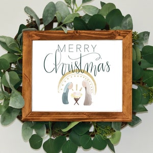 Puede incluir: Una impresión enmarcada con el texto "Feliz Navidad" en una fuente cursiva. La impresión presenta una ilustración de acuarela de la escena de la Natividad con María, José y el bebé Jesús en un pesebre.