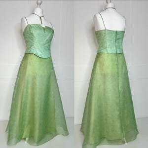 May include: A two-piece green formal dress. The bodice is a lighter green with a sweetheart neckline and spaghetti straps. The skirt is a flowing, darker green, floor-length design. The dress is displayed on a mannequin.
