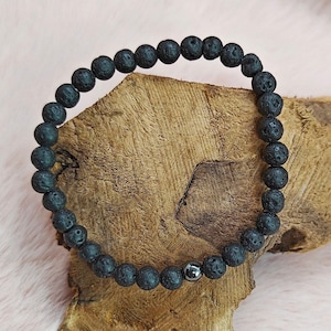 Könnte beinhalten: Ein Armband aus schwarzen Lavasteinen mit einer einzelnen silbernen Perle.
