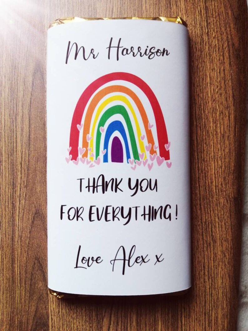 Op de afbeelding: Witte chocoladereepverpakking met een regenboogontwerp en de tekst "Mr Harrison, Bedankt voor alles! Love Alex x". De regenboog heeft rode, oranje, gele, groene, blauwe en paarse bogen met roze hartjes.