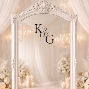 May include: A white, ornate framed mirror with the letters "K&G" in black. The mirror is set in a room with white flowers, candles, and chandeliers, creating a romantic and elegant atmosphere.