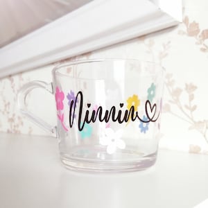 May include: Clear plastic cup with a floral design and the word "Minnin" written in black cursive. The cup has a handle and a heart symbol next to the name.