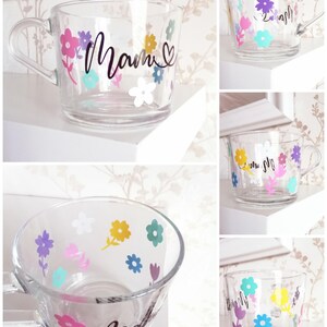 May include: A clear glass mug with a black floral design and the word "Mamm" written on it. The mug is decorated with colorful flowers.