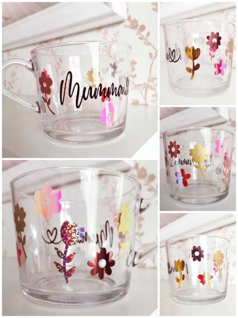 May include: A clear glass mug with a handle decorated with colorful flowers and glitter. The mug has the word "Mumma" written on it in black.