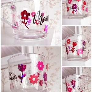 May include: A clear glass mug with a handle decorated with pink and red flowers and the word "Mama" in black lettering.