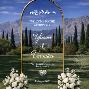 May include: An arched gold-framed wedding sign with white text reading "WELCOME TO THE WEDDING OF Yasser & Veronica", "And He placed between you love and mercy", and "7thAugust 2026", featuring Arabic calligraphy and two white floral arrangements.