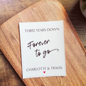 Pu&ograve; includere: Carta bianca con testo nero che dice "Three Years Down Forever to go Charlotte & Travis" con un simbolo di cuore rosso.