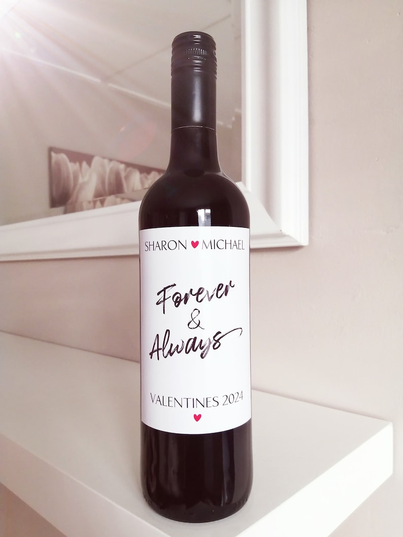 Pu&ograve; includere: Una bottiglia di vino rosso con un'etichetta bianca che dice "Sharon &hearts; Michael Forever & Always Valentines 2024" con un piccolo cuore rosso in basso.