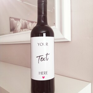 Pu&ograve; includere: Una bottiglia di vino rosso con un'etichetta bianca che dice "YOUR Text HERE" con un cuore rosa.