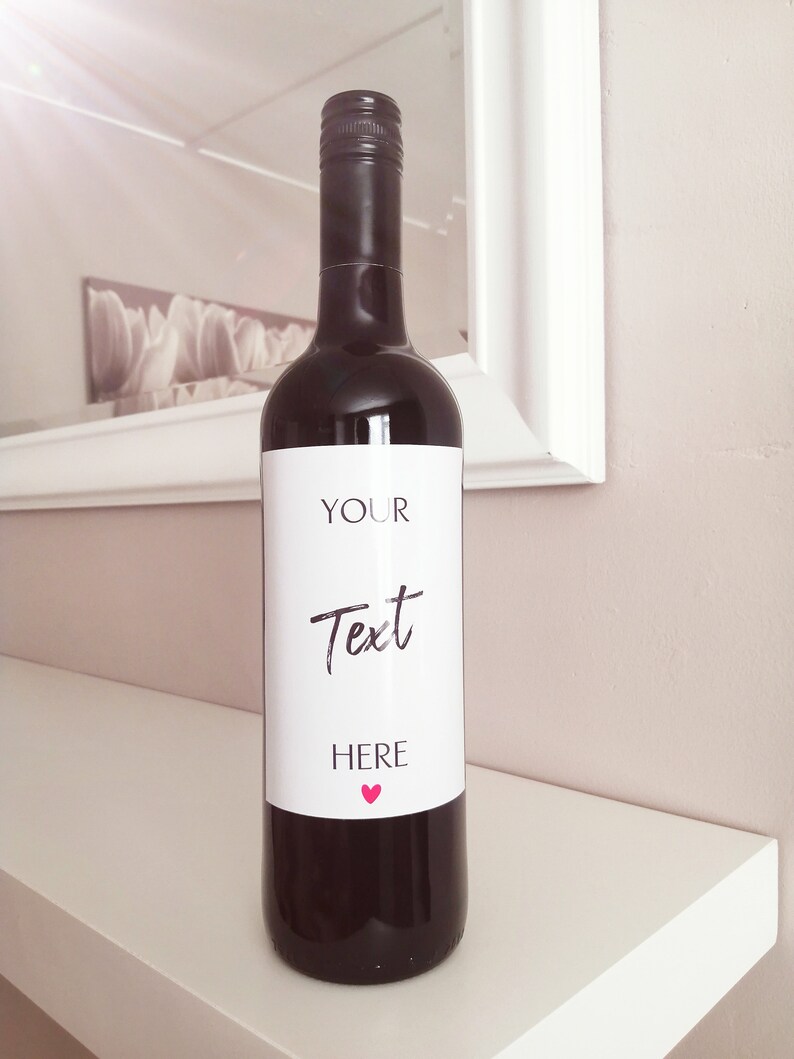 Pu&ograve; includere: Una bottiglia di vino rosso con un'etichetta bianca che dice "YOUR Text HERE" con un cuore rosa.