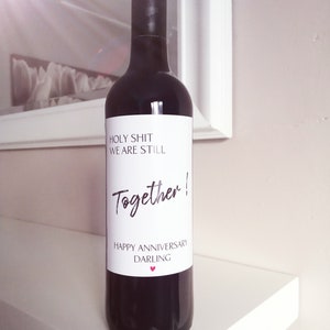 Pu&ograve; includere: Una bottiglia di vino rosso con un'etichetta bianca che dice "Holy Shit We Are Still Together! Happy Anniversary Darling".