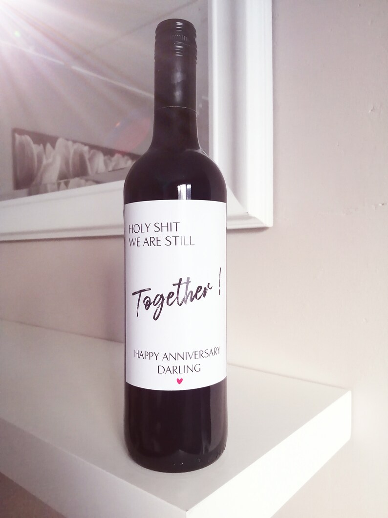 Pu&ograve; includere: Una bottiglia di vino rosso con un'etichetta bianca che dice "Holy Shit We Are Still Together! Happy Anniversary Darling".