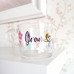May include: A clear glass mug with a black floral design and the word "Gran" in black script with a heart.