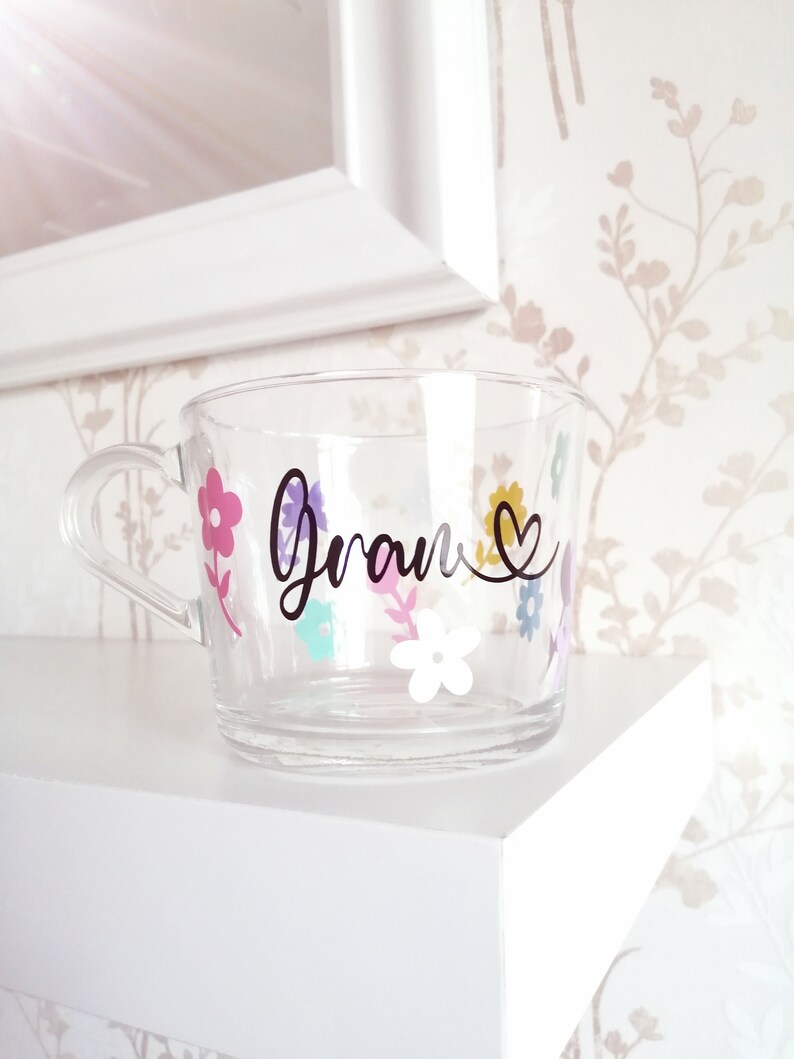 May include: A clear glass mug with a black floral design and the word "Gran" in black script with a heart.