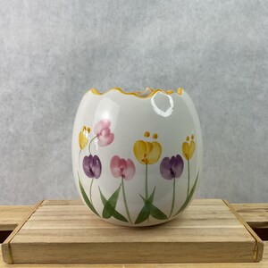 May include: A white ceramic vase with a scalloped rim and hand-painted tulip design. The tulips are in shades of yellow, pink, and purple with green stems and leaves. The rim is trimmed with gold.