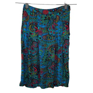 May include: A knee-length skirt with a vibrant paisley pattern in shades of blue, teal, red, and yellow. The skirt is hanging from a metal hanger against a white background. The fabric appears to be lightweight.