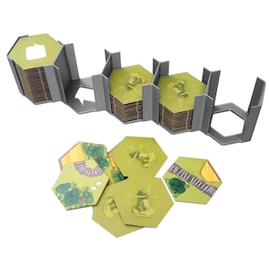 Puede incluir: Un organizador de plástico gris con cinco ranuras para guardar fichas de juego hexagonales. El organizador está vacío, pero hay seis fichas hexagonales verdes y amarillas con varios diseños.
