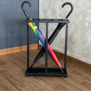 May include: Black metal umbrella stand with two umbrellas, one black and one with rainbow stripes, standing inside.