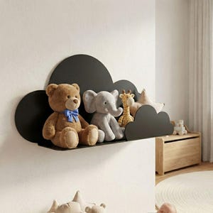Op de afbeelding: Een zwart, wolkvormig rek aan een witte muur met knuffels. Een bruine teddybeer met een blauwe strik, een grijze olifant en een giraf zijn zichtbaar. Een stervormig kussen en ander speelgoed zijn ook aanwezig.