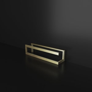 May include: A gold-colored metal frame with a rectangular shape. The frame is made of two pieces of metal that are joined together at the corners. The frame is sitting on a black surface.