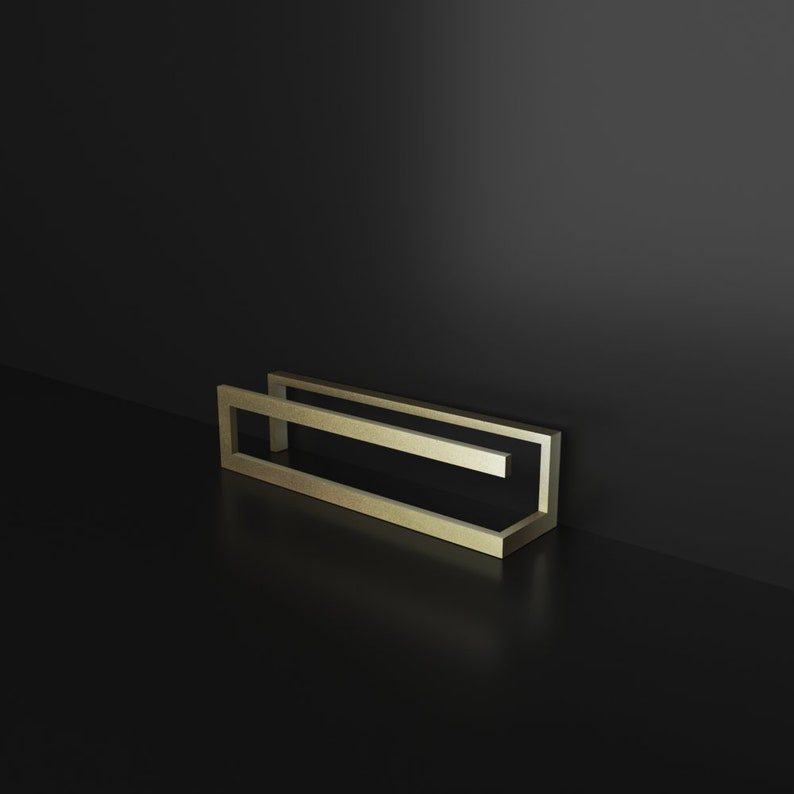 May include: A gold-colored metal frame with a rectangular shape. The frame is made of two pieces of metal that are joined together at the corners. The frame is sitting on a black surface.