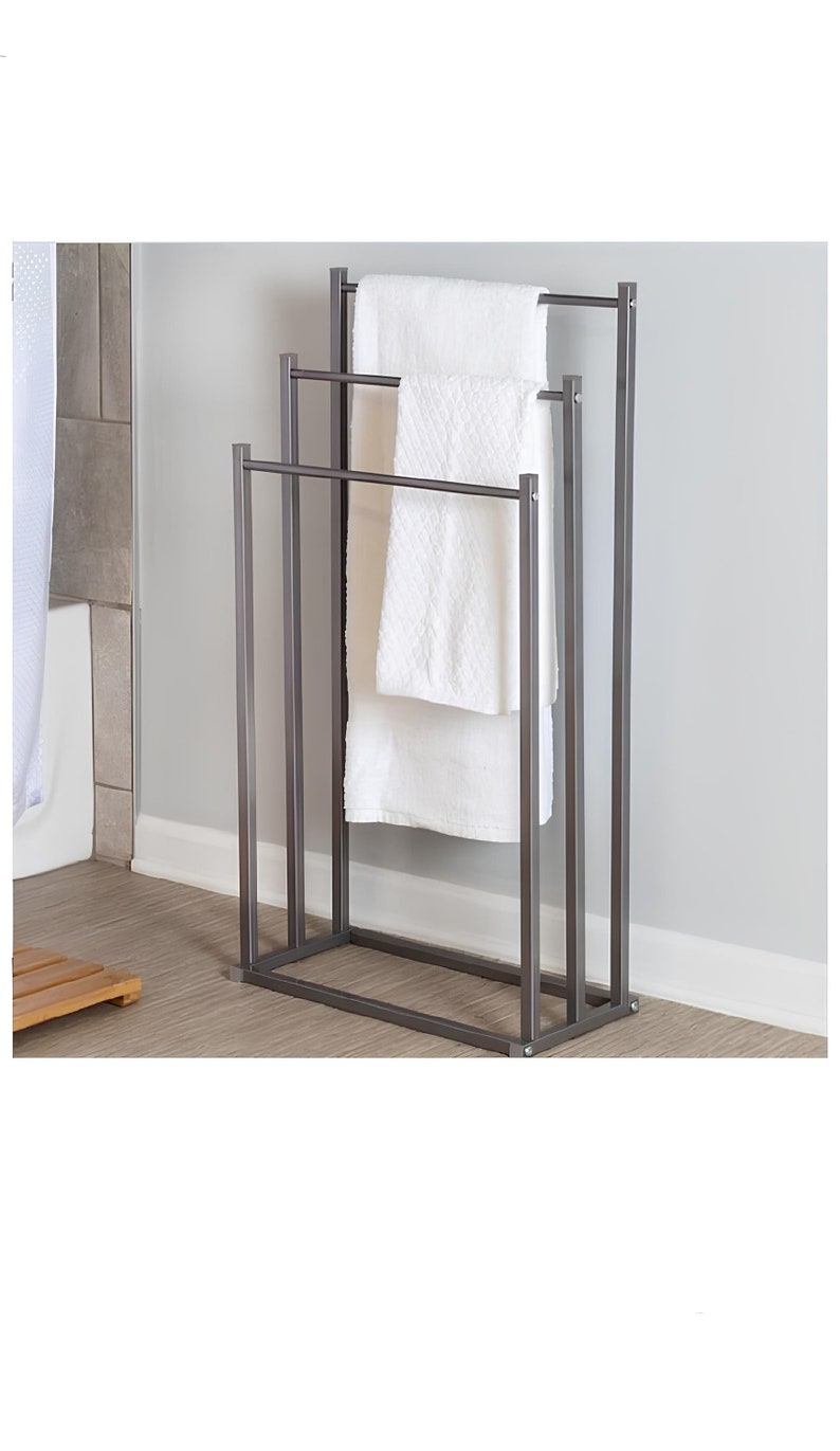 May include: A three-tiered towel rack made of metal with a dark grey finish. The rack has three horizontal bars for hanging towels and a rectangular base.