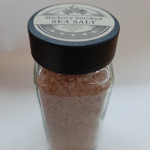 May include: A glass jar filled with pink Himalayan sea salt, labeled "Hickory Smoked Sea Salt". The label has a vintage design with stars and the words "Ingredients: Pink Himalayan Sea Salt".
