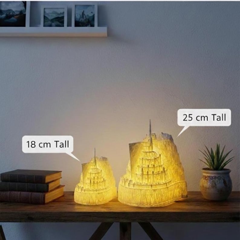 May include: Two illuminated, off-white, castle-shaped lamps with intricate architectural details. The smaller lamp is 18 cm tall, and the larger lamp is 25 cm tall. Both emit a warm, soft yellow glow from within, highlighting the textured structure.