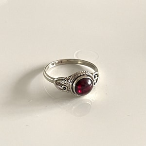 Könnte beinhalten: Ein silberner Ring mit einem verzierten Design und einem roten Edelstein.