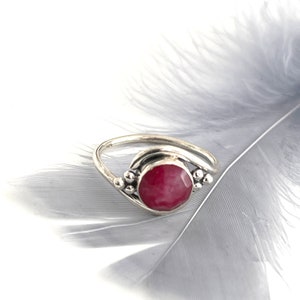 Könnte beinhalten: Ein silberner Ring mit einem rosafarbenen Edelstein, der in einem gebogenen Band gefasst ist. Der Ring ist an beiden Seiten des Steins mit kleinen silbernen Perlen verziert.