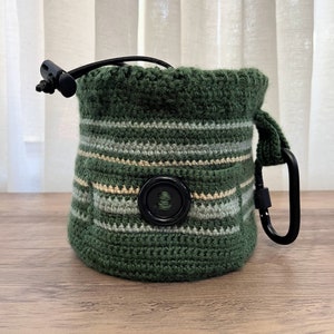 May include: A green crocheted drawstring bag with a black button and a black carabiner clip.
