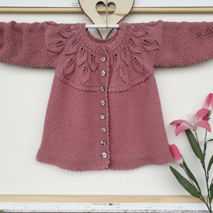May include: A dusty rose knitted cardigan with a delicate leaf pattern around the neckline and button closure.