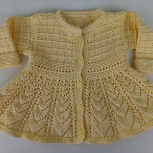 May include: A pale yellow knitted cardigan with a button-up front and a scalloped hem. The cardigan has a delicate lace pattern throughout.