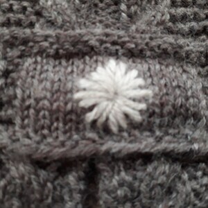 May include: A close-up of a gray knitted fabric with a white embroidered flower design.