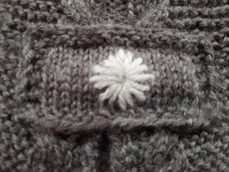 May include: A close-up of a gray knitted fabric with a white embroidered flower design.