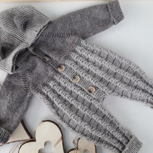 May include: A gray knitted baby onesie with a hood and buttons. The onesie has a cable knit pattern and is made of soft yarn.