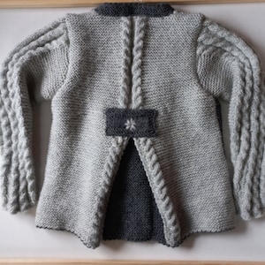 May include: A gray knitted cardigan with a gray and black flower design on the back. The cardigan has long sleeves with a cable knit pattern.