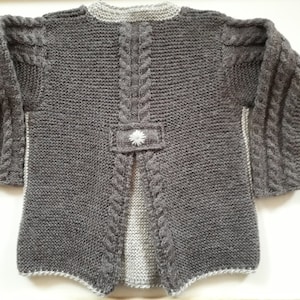 May include: Gray knitted cardigan with a white flower detail on the back. The cardigan has a cable knit pattern and a split back.