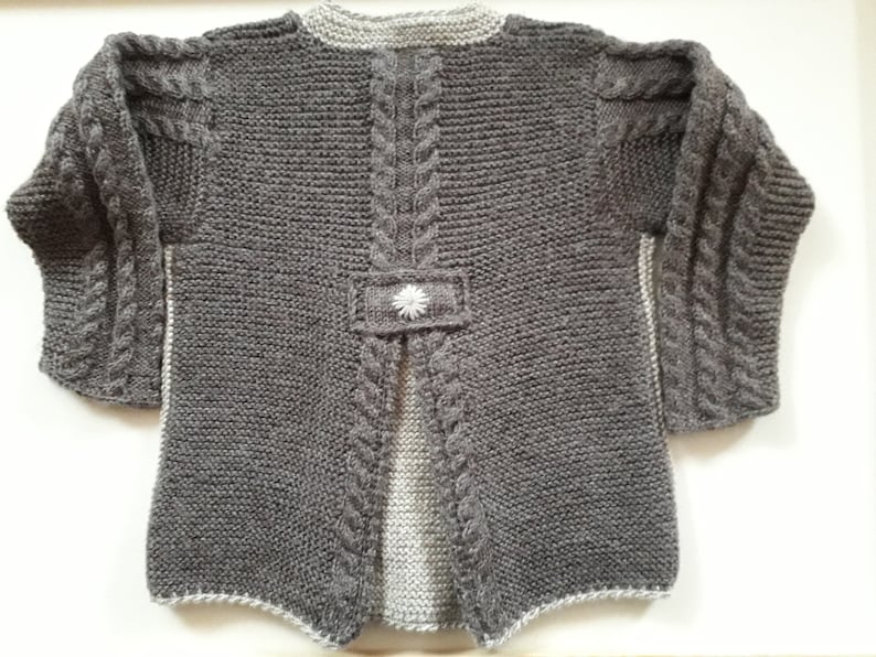 May include: Gray knitted cardigan with a white flower detail on the back. The cardigan has a cable knit pattern and a split back.