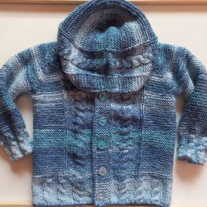 Könnte beinhalten: Ein gestrickter Cardigan in Blau- und Weißstreifen mit Kapuze und Knopfleiste. Der Cardigan hat ein Zopfmuster und ist aus weichem Garn gefertigt.