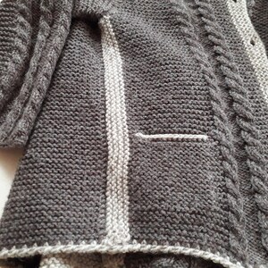 May include: A gray knitted cardigan with a white stripe down the front and a cable knit pattern on the sleeves.
