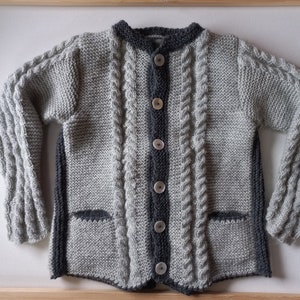 May include: A gray and black knitted cardigan with a cable knit pattern and button closure. The cardigan has two pockets.