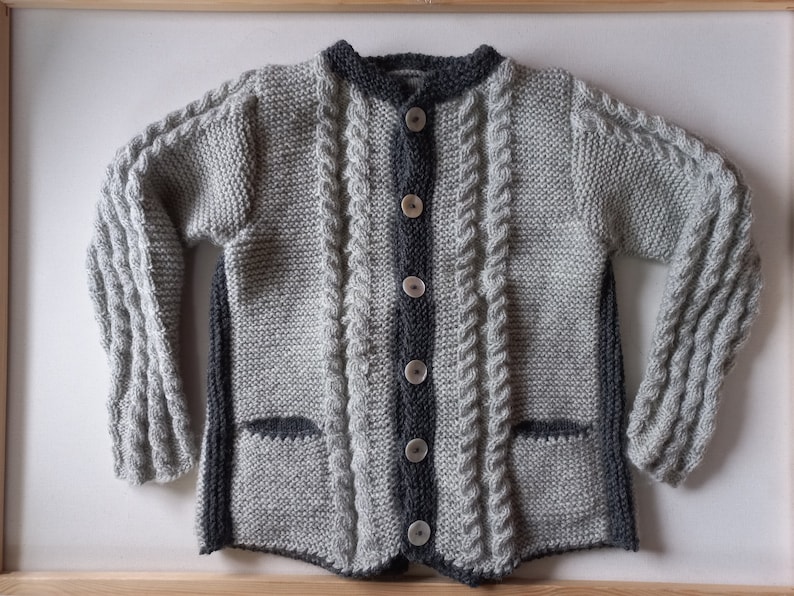 May include: A gray and black knitted cardigan with a cable knit pattern and button closure. The cardigan has two pockets.